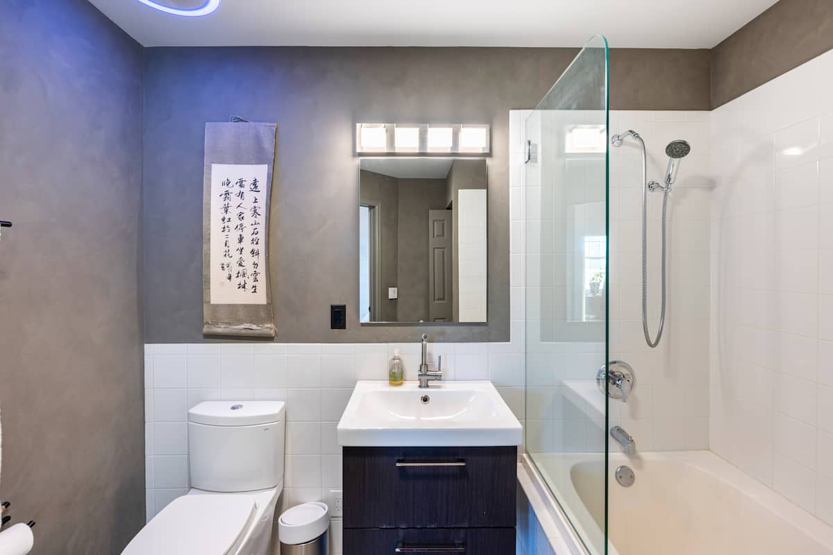 Master bathroom with a deep soaking tub, glass shower enclosure, and white tile in the furnished Belvedere Tower residence.
