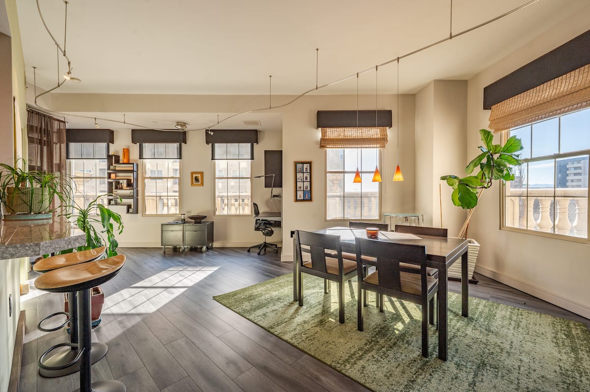 Open-plan living and dining area of The Observatory at The Belvedere Tower, with hardwood floors and seven oversized windows filling the furnished Denver residence with daylight.